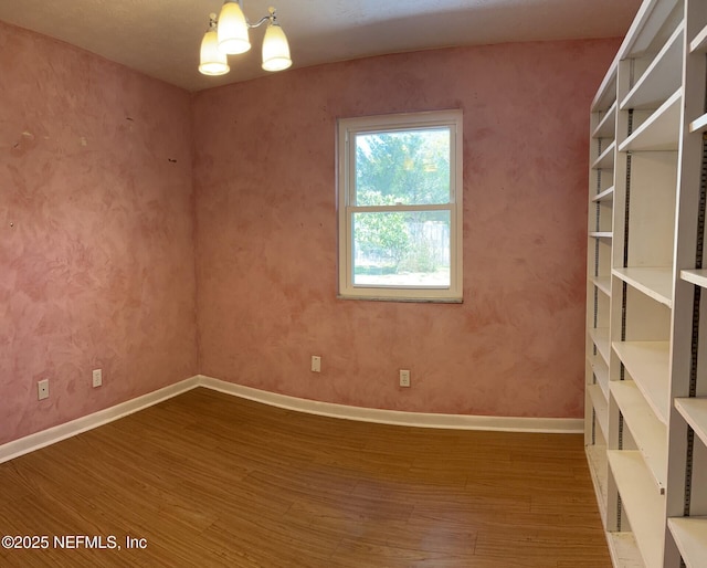 unfurnished room featuring a notable chandelier, baseboards, and wood finished floors