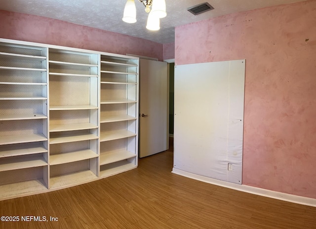 unfurnished bedroom with a textured ceiling, wood finished floors, visible vents, and baseboards