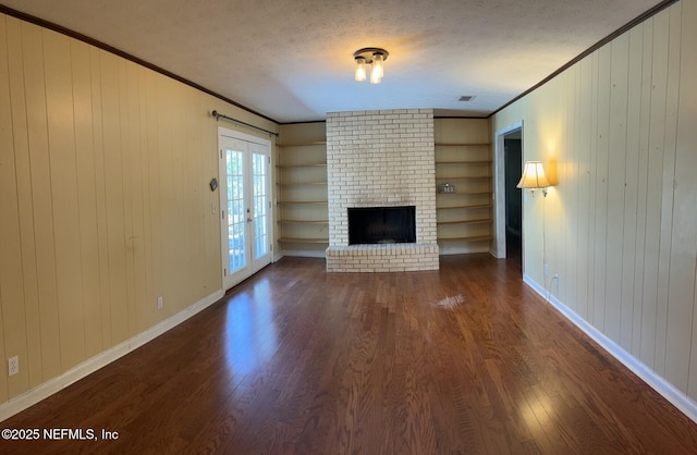 unfurnished living room featuring built in shelves, crown molding, dark wood-type flooring, a brick fireplace, and a textured ceiling