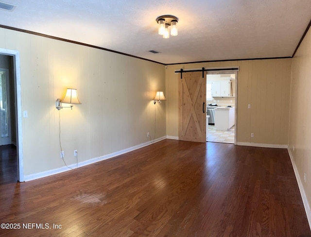 empty room with ornamental molding, wood finished floors, visible vents, and a barn door