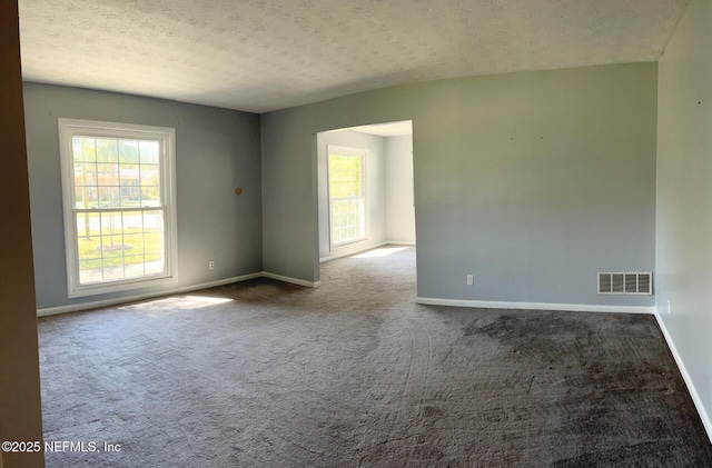 unfurnished room with a textured ceiling, dark carpet, visible vents, and baseboards