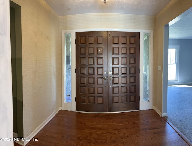 carpeted foyer with baseboards, a textured ceiling, wood finished floors, and wallpapered walls