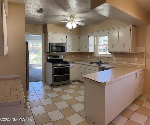 kitchen featuring visible vents, tile counters, decorative backsplash, appliances with stainless steel finishes, and a sink