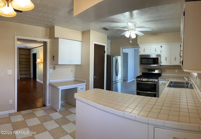 kitchen featuring stainless steel appliances, tile counters, a sink, a textured ceiling, and a peninsula