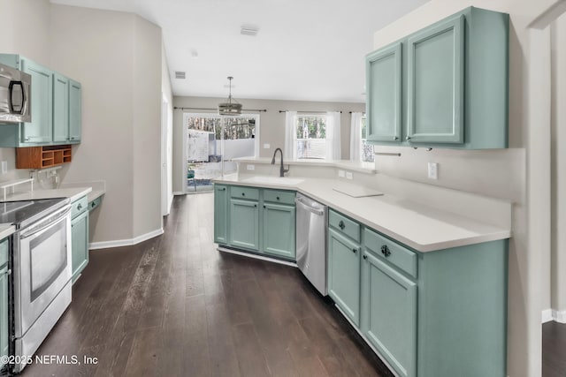 kitchen featuring a sink, dark wood finished floors, appliances with stainless steel finishes, a peninsula, and light countertops