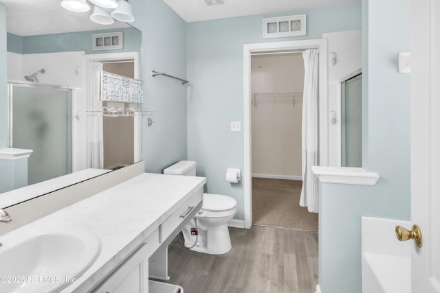 full bath featuring a walk in closet, vanity, wood finished floors, and a shower stall