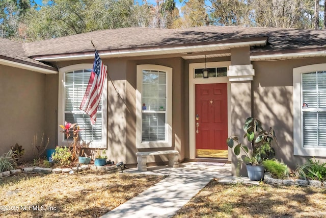 doorway to property with stucco siding and roof with shingles