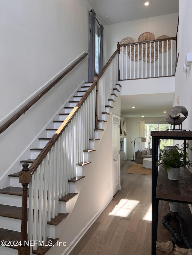 stairs with recessed lighting, a towering ceiling, baseboards, and wood finished floors