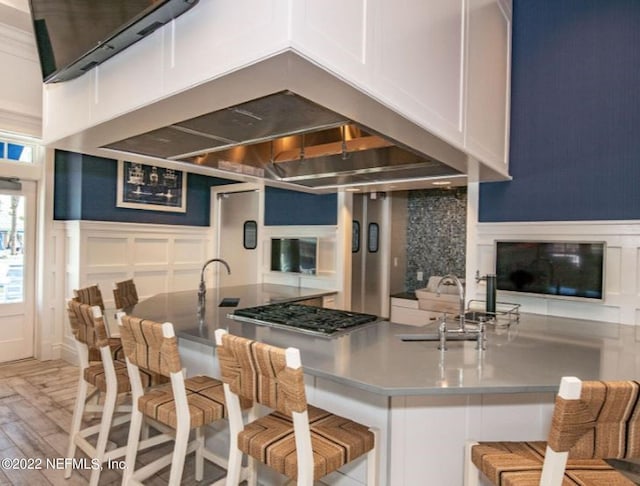 kitchen with white cabinetry, a breakfast bar area, light wood-style flooring, and a decorative wall