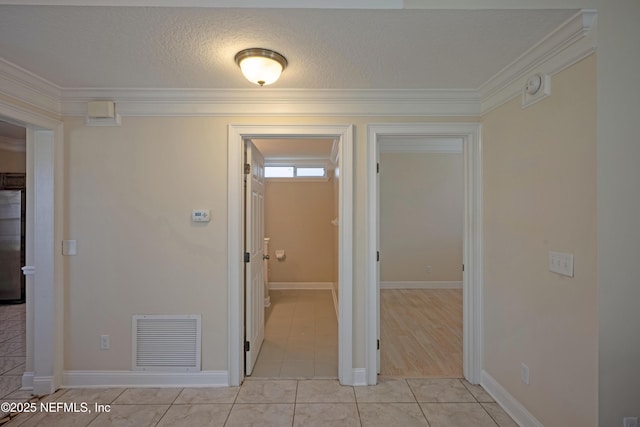 corridor featuring a textured ceiling, light tile patterned flooring, visible vents, and crown molding