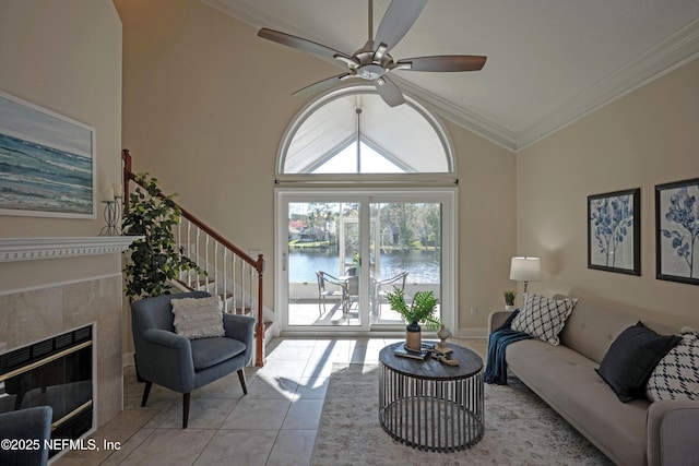 living area with a water view, ornamental molding, a ceiling fan, tile patterned flooring, and a tile fireplace