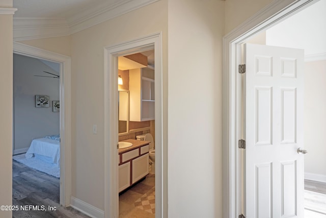 corridor featuring light floors, ornamental molding, a sink, and baseboards