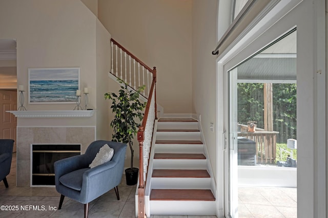 stairway with a high ceiling, a tiled fireplace, tile patterned flooring, and a healthy amount of sunlight