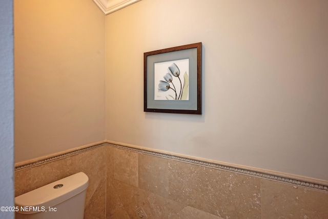 bathroom with wainscoting, toilet, and tile walls