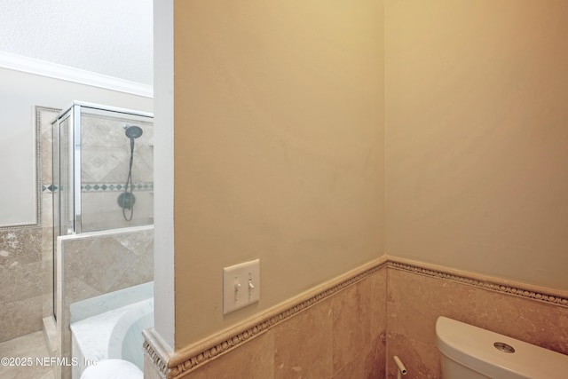 bathroom featuring a washtub, tile walls, toilet, a stall shower, and wainscoting