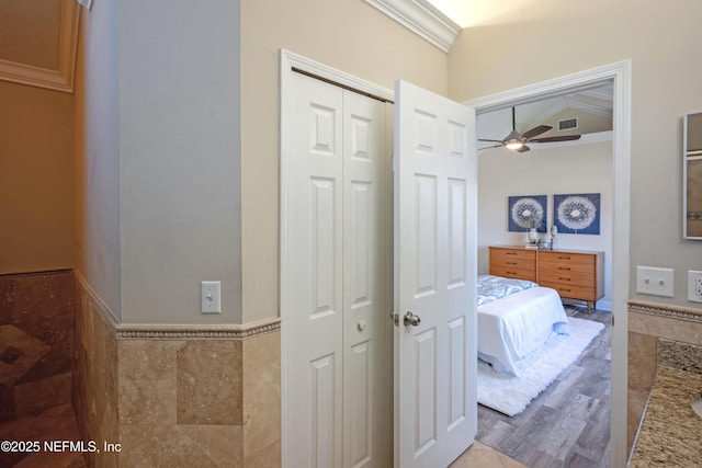 full bath featuring a closet, visible vents, a ceiling fan, crown molding, and tile walls