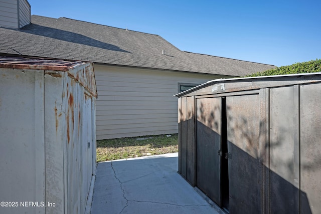 view of side of home with a storage shed, a shingled roof, and an outdoor structure