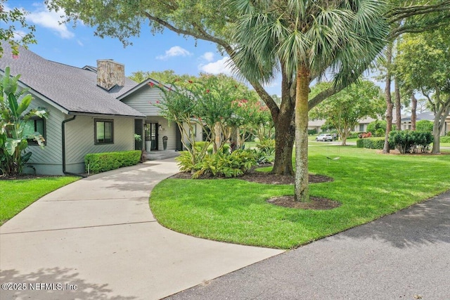 view of front of house with driveway, a chimney, a front yard, and a shingled roof