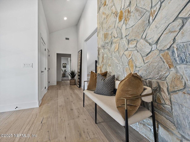 hall featuring visible vents, baseboards, light wood finished floors, and high vaulted ceiling