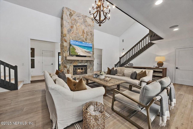 living area with a high ceiling, a fireplace, stairs, light wood-style floors, and a chandelier