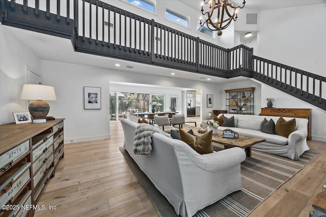 living room featuring visible vents, wood-type flooring, a high ceiling, an inviting chandelier, and baseboards