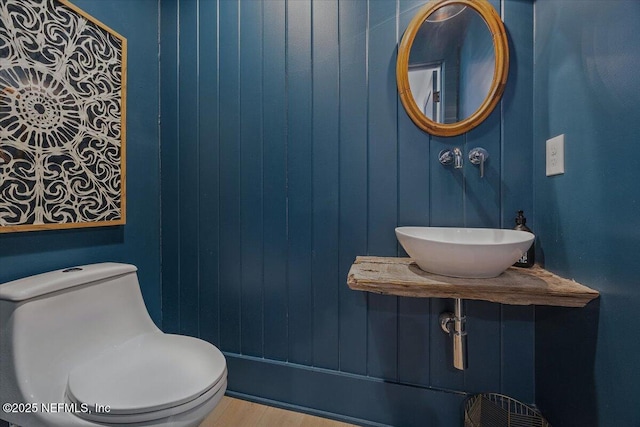 half bathroom featuring toilet, wood finished floors, and a sink