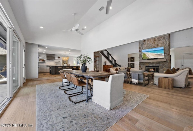 dining room with a ceiling fan, light wood-style flooring, stairs, and a fireplace