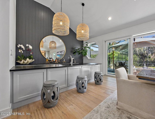 interior space featuring wooden walls, a sink, vaulted ceiling, light wood-style floors, and decorative light fixtures