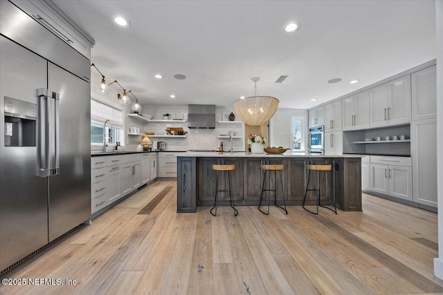 kitchen featuring plenty of natural light, wall chimney exhaust hood, stainless steel built in fridge, and open shelves