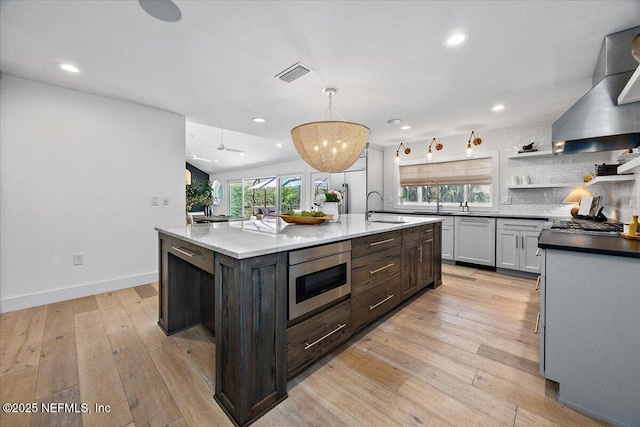 kitchen featuring stainless steel microwave, light wood-style flooring, wall chimney exhaust hood, and visible vents