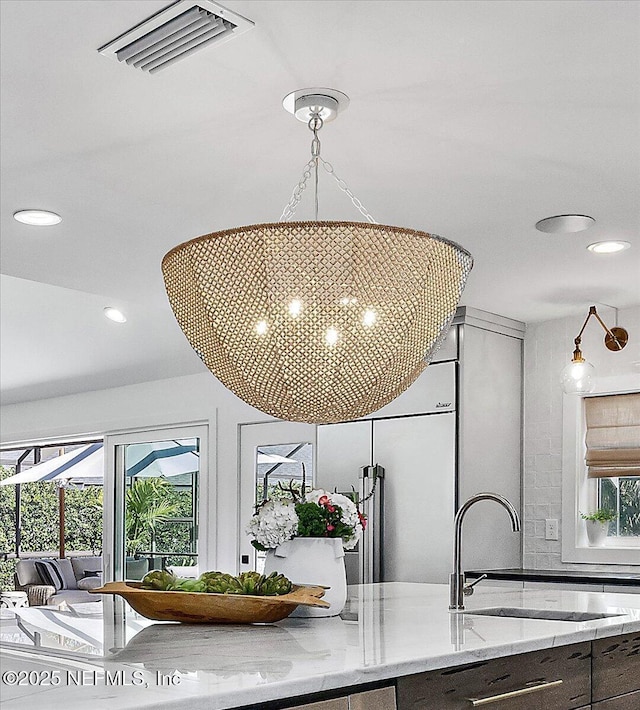 room details with visible vents, a sink, light stone counters, recessed lighting, and an inviting chandelier