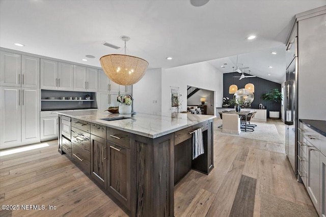 kitchen featuring pendant lighting, light wood-style flooring, a sink, a spacious island, and lofted ceiling