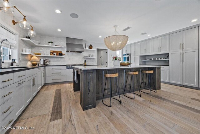 kitchen with light wood-style flooring, open shelves, a sink, wall chimney range hood, and stainless steel oven