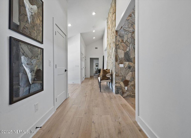 hallway featuring light wood finished floors, recessed lighting, high vaulted ceiling, and baseboards