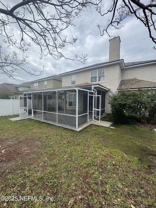 rear view of property with stucco siding, fence, a chimney, and a lawn