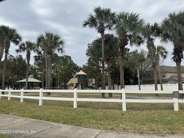 view of property's community with playground community, a lawn, and fence