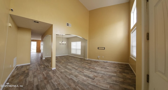 spare room with arched walkways, dark wood-style flooring, a towering ceiling, and visible vents