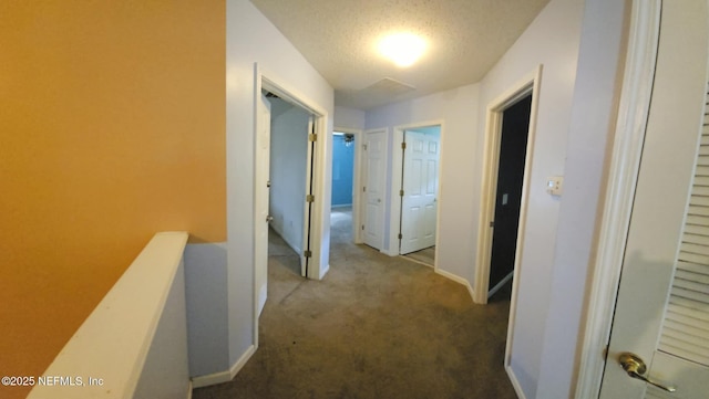 hall featuring carpet, baseboards, a textured ceiling, and an upstairs landing