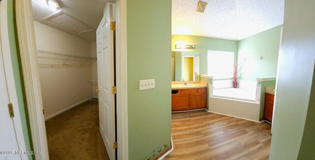 bathroom with wood finished floors, a walk in closet, a textured ceiling, vanity, and a bath