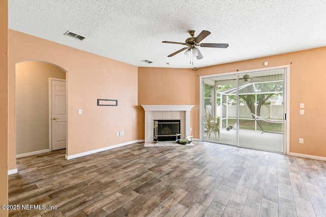 3925 Leatherwood Dr, Orange Park, FL 32065 - unfurnished living room with a ceiling fan, arched walkways, wood finished floors, a textured ceiling, and a tiled fireplace