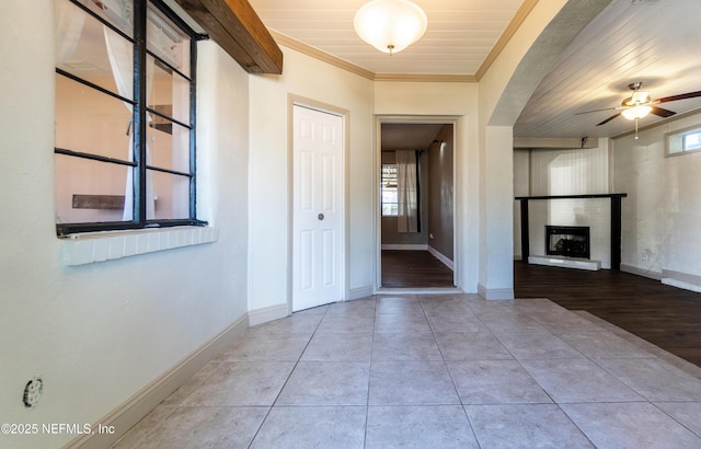 tiled foyer featuring baseboards, ceiling fan, a fireplace, and crown molding