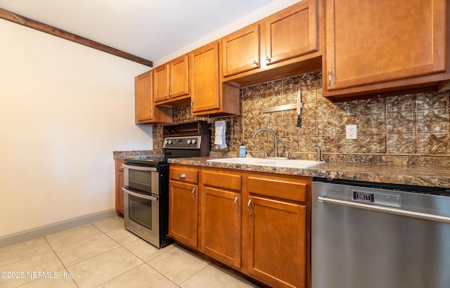 kitchen featuring light tile patterned floors, stainless steel appliances, decorative backsplash, brown cabinetry, and a sink