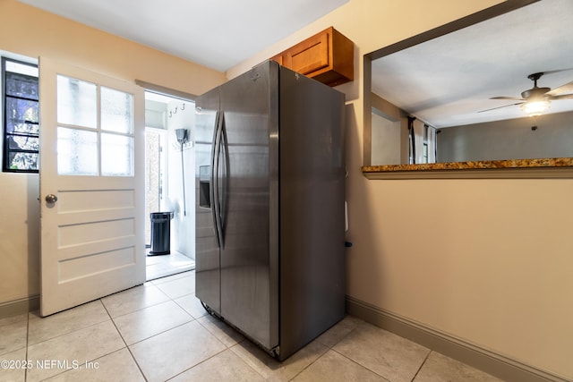 kitchen with ceiling fan, light tile patterned flooring, baseboards, brown cabinetry, and stainless steel fridge