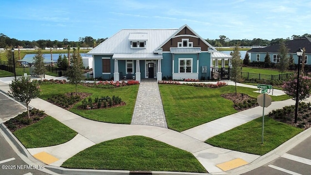 view of front of home with a front yard, fence, a standing seam roof, a water view, and metal roof