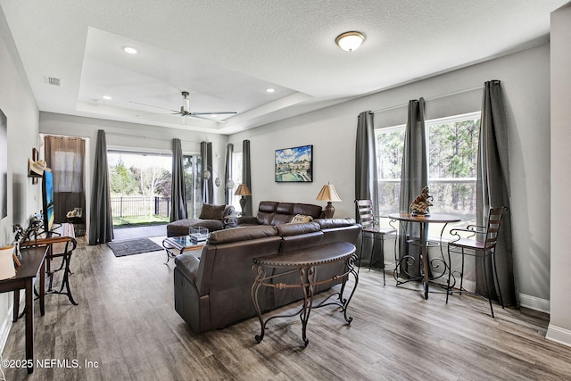 living room featuring ceiling fan, baseboards, a raised ceiling, and wood finished floors