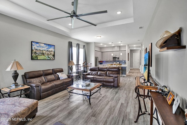 living area with light wood finished floors, visible vents, recessed lighting, a raised ceiling, and a ceiling fan