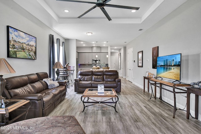 living room with a raised ceiling, a ceiling fan, baseboards, and light wood finished floors