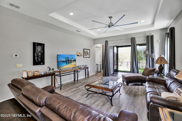 living room with a tray ceiling, baseboards, wood finished floors, and a ceiling fan