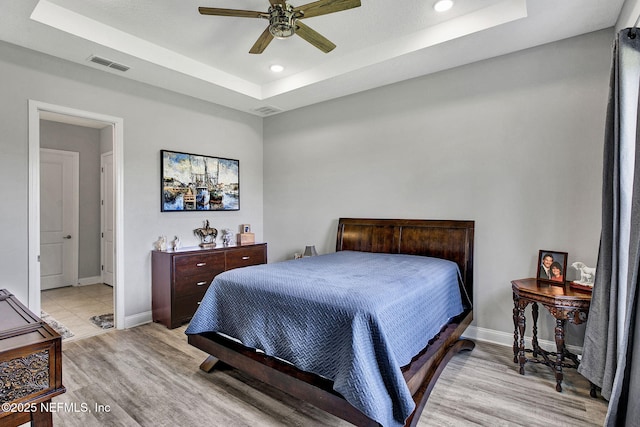 bedroom featuring a tray ceiling, baseboards, visible vents, and light wood finished floors