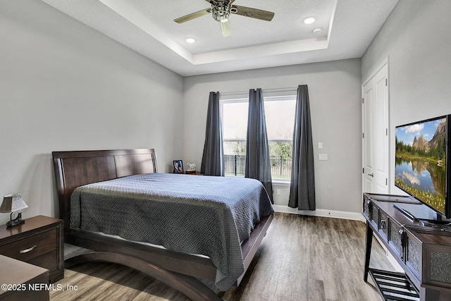 bedroom with recessed lighting, baseboards, a tray ceiling, and wood finished floors